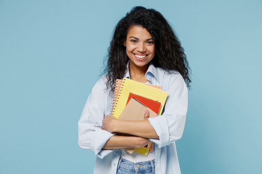 Young smiling smart nerd african american girl teen student wear denim clothes holding books prepare for exam notebook isolated on blue background Education in high school university college concept.