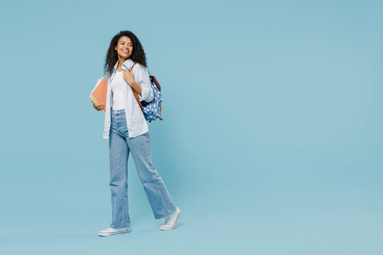 Full length young happy african american girl teen student wear denim clothes backpack hold books walk isolated on blue background studio portrait Education in high school university college concept