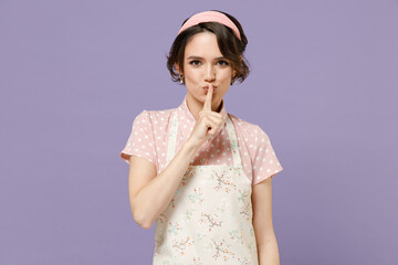 Young insighted housewife housekeeper chef cook baker woman wear pink apron t-shirt say hush be quiet with finger on lips shhh gesture isolated on pastel violet background studio Cooking food concept