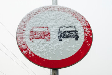 Znak zakazu wyprzedzania pojazdów w warunkach zimowych, pokryty śniegiem - obrazy, fototapety, plakaty