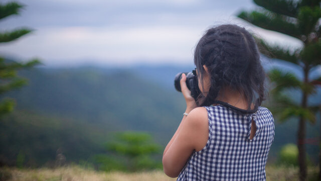 Little child girl taking photo of beautiful landscape.She standing on hill with background of mountains
