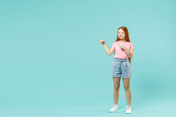 Obraz na płótnie Canvas Full length little redhead kid girl 12-13 year old in pink striped t-shirt point index finger aside on copy space mock up area isolated on pastel blue background Children lifestyle childhood concept.