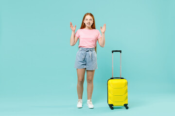 Full length traveler tourist kid girl 12-13 years old in pink t-shirt hold suitcase spread hands isolated on pastel blue background Passenger travel abroad weekends getaway Air flight journey concept