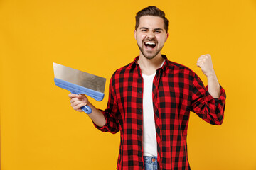 Young employee handyman man in checkered shirt hold putty knife do winner gesture clench fist...