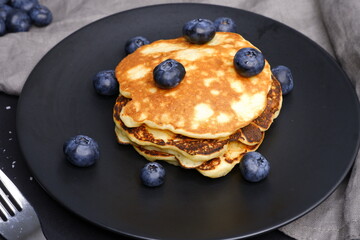 Pancakes with blueberries on a black background and in a black plate.