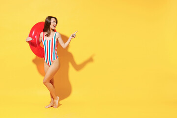 Fototapeta na wymiar Full length fun happy young sexy woman slim body wear red blue swimsuit pose go with inflatable rubber ring isolated on vivid yellow color background studio Summer hotel pool sea rest sun tan concept