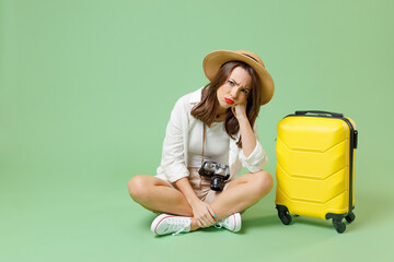 Full length sad troubled traveler tourist woman in casual clothes hat suitcase sitting prop up...