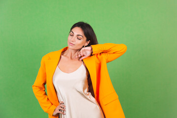 Stylish woman in silk beige dress and orange oversized blazer on green background, positive emotions smile