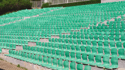 Fototapeta premium Lots of empty seats in old open-air theater theater. Plastic green seats are arranged in a rows.