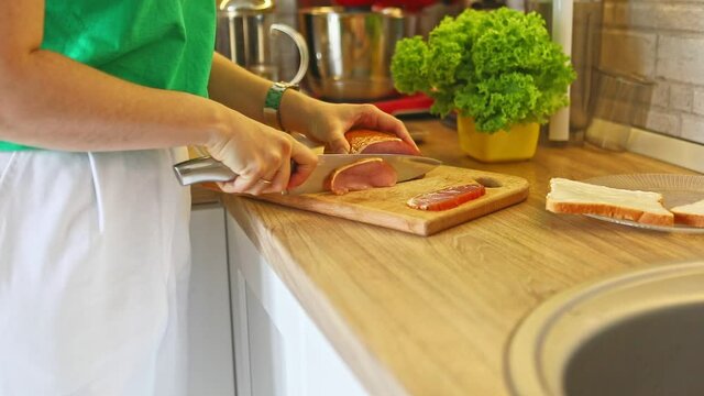 woman slicing meat on cut board at the kitchen making sandwiches