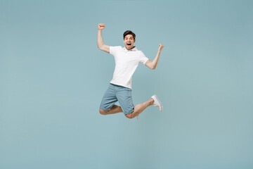 Full length young fun happy caucasian man 20s wear white casual basic t-shirt do winner gesture clench fist jump high isolated on pastel blue color background studio portrait People lifestyle concept