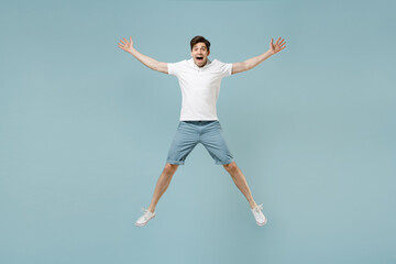Full length young fun happy caucasian man 20s wearing white casual basic t-shirt jump high with outstretched hands isolated on pastel blue color background studio portrait. People lifestyle concept.