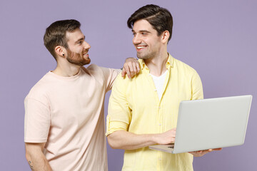 Young fun cool smiling happy men friends together wear casual t-shirt hold laptop pc computer look to each other hug isolated on purple background studio portrait People lifestyle friendship concept.