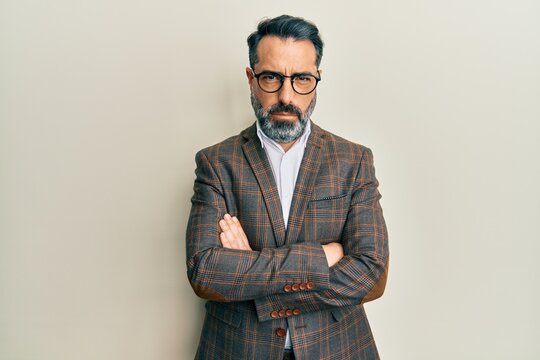 Middle age man with beard and grey hair wearing business jacket and glasses skeptic and nervous, disapproving expression on face with crossed arms. negative person.