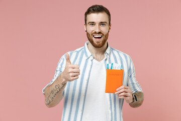 Fototapeta premium Traveler tourist man in striped shirt hold passport ticket show thumb up isolated on pastel pink background. Passenger travel abroad weekends getaway. Air flight journey concept. Tattoo translate fun