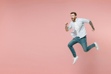 Fototapeta na wymiar Full length side view sporty young caucasian unshaven man 20s wearing blue striped shirt white t-shirt jump high run fast hurry up isolated on pastel pink color background. People lifestyle concept.