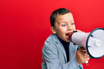 Adorable caucasian boy screaming using megaphone over isolated red background.