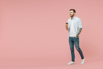 Fototapeta na wymiar Full length of young unshaven man 20s wearing blue striped shirt hold takeaway delivery craft paper brown cup coffee to go walk isolated on pastel pink background studio portrait Tattoo translate fun