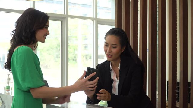 Business woman arrive to hotel check in by application on smart phone taking room key card by asian receptionist registration at reception hotel . female Guest check in by app online hotel booking