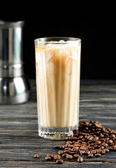 Iced coffee with ice and milk in a tall glass on a black wooden background.