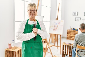 Two senior paint student smiling happy painting at art studio. Woman standing with smile on face holding paintbrushes.