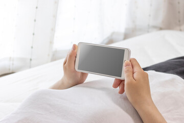 寝ながらスマートフォンを使う女性の手元（日本人、若い、30代）