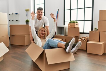 Young caucasian couple smiling happy playing with cardboard box as a car at new home.