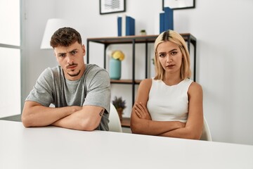 Fototapeta premium Young beautiful couple wearing casual clothes sitting on the table at home skeptic and nervous, disapproving expression on face with crossed arms. negative person.