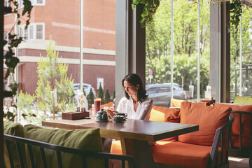 The girl is sitting in a cafe, restaurant, resting, relaxing, looking out the window, drinking tea.