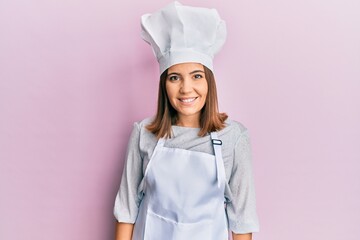 Young beautiful woman wearing professional cook uniform and hat with a happy and cool smile on...