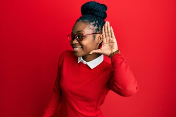 Young african american woman wearing casual clothes and glasses smiling with hand over ear listening an hearing to rumor or gossip. deafness concept.