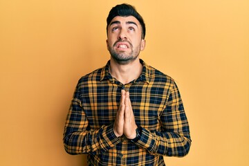 Young hispanic man wearing casual clothes begging and praying with hands together with hope expression on face very emotional and worried. begging.