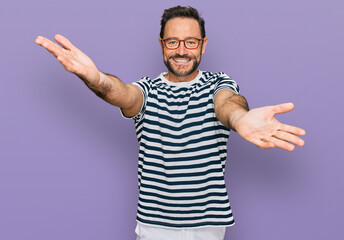 Naklejka premium Middle age man wearing casual clothes and glasses looking at the camera smiling with open arms for hug. cheerful expression embracing happiness.