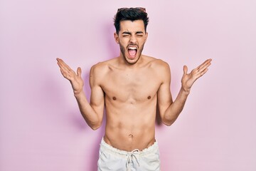 Young hispanic man wearing swimwear shirtless celebrating mad and crazy for success with arms...