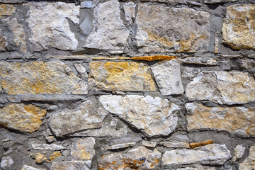 An old stone wall texture. Grey color stones with yellow tint of different sizes and shapes background.