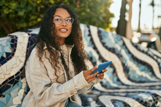 Young latin woman smiling happy using touchpad sitting on the bench at the city.