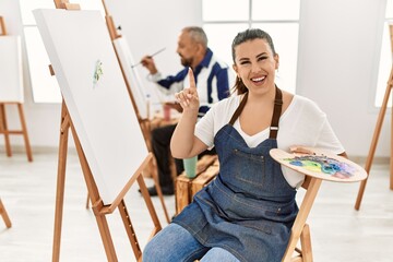 Young artist woman at art studio surprised with an idea or question pointing finger with happy face, number one