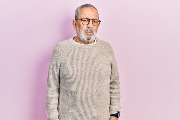 Handsome senior man with beard wearing casual sweater and glasses relaxed with serious expression on face. simple and natural looking at the camera.