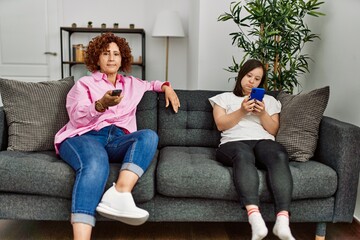 Mature mother and down syndrome daughter at home watching television and using smartphone
