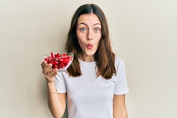 Young brunette woman holding red peppers scared and amazed with open mouth for surprise, disbelief face