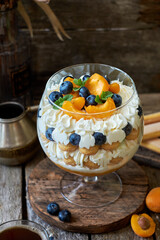 Apricot trifle with blueberries, cookies and cream cheese. Wooden background, side view