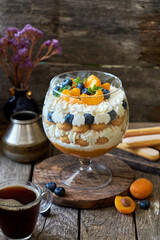 Apricot trifle with blueberries, cookies and cream cheese. Wooden background, side view
