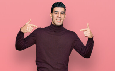 Fototapeta premium Handsome hispanic man wearing casual turtleneck sweater looking confident with smile on face, pointing oneself with fingers proud and happy.