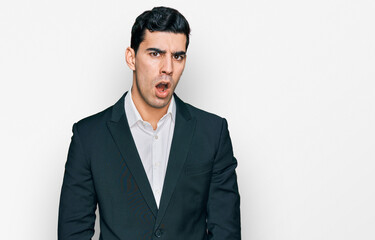 Handsome hispanic man wearing business clothes in shock face, looking skeptical and sarcastic, surprised with open mouth