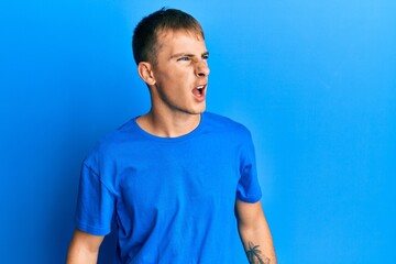 Young caucasian man wearing casual blue t shirt angry and mad screaming frustrated and furious, shouting with anger. rage and aggressive concept.
