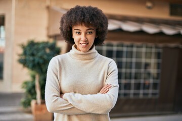 Young hispanic girl with arms crossed smiling happy at the city.