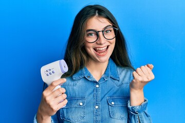 Young caucasian woman holding digital thermometer screaming proud, celebrating victory and success...