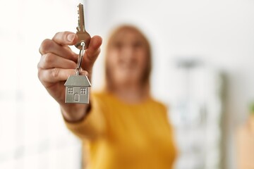 Middle age blonde woman smiling happy holding key of new home.