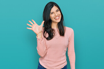Young hispanic woman wearing casual clothes showing and pointing up with fingers number five while...