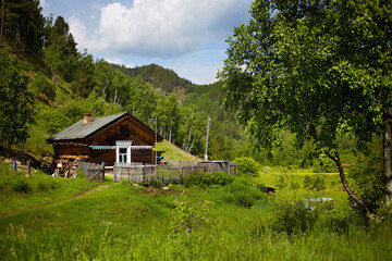 An old country house in the middle of a forest and mountains on a warm summer day. Seclusion, rural life.
